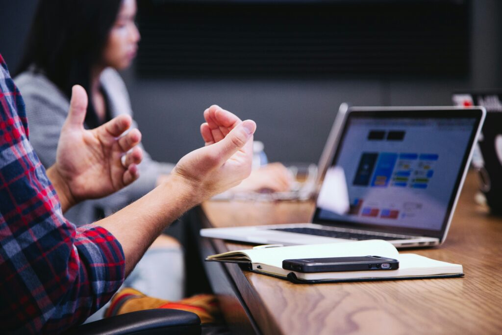 Two professionals engaged in a marketing partnership meeting at a wooden conference table, with one person in a plaid shirt gesturing expressively while discussing strategy.